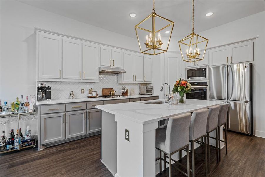 Kitchen with hanging light fixtures, a center island with sink, sink, appliances with stainless steel finishes, and dark hardwood / wood-style flooring