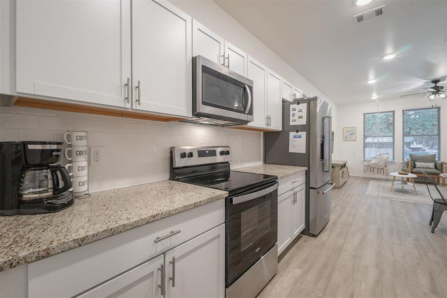 Kitchen with appliances with stainless steel finishes, white cabinets, backsplash, light stone countertops, and light wood-type flooring