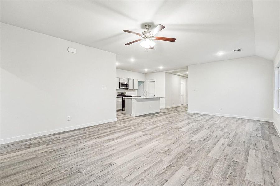 Unfurnished living room with sink, vaulted ceiling, ceiling fan, and light wood-type flooring