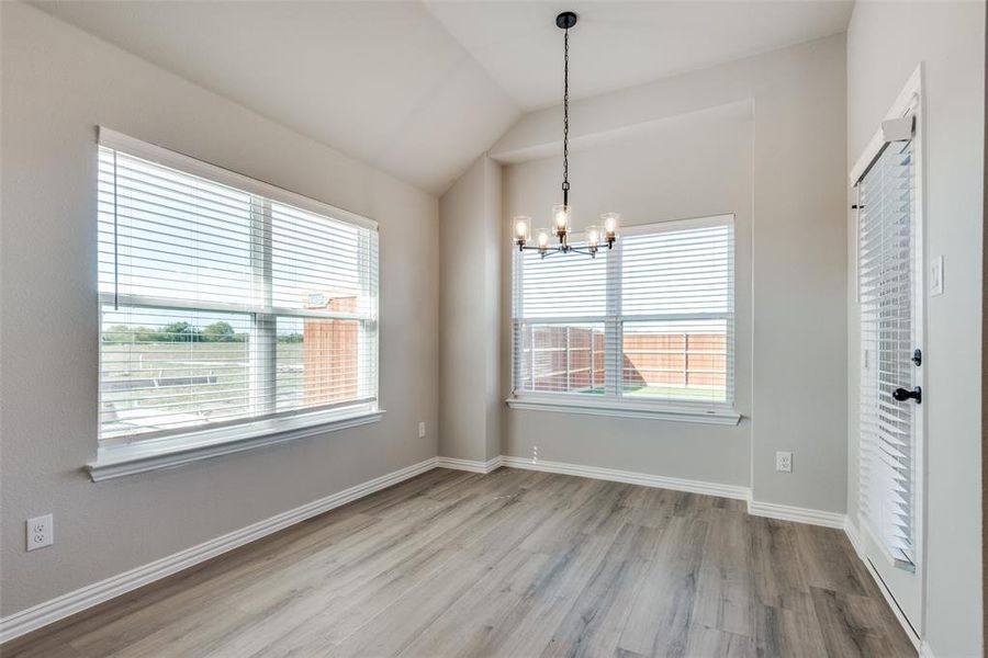 Unfurnished dining area featuring an inviting chandelier, light hardwood / wood-style flooring, and vaulted ceiling