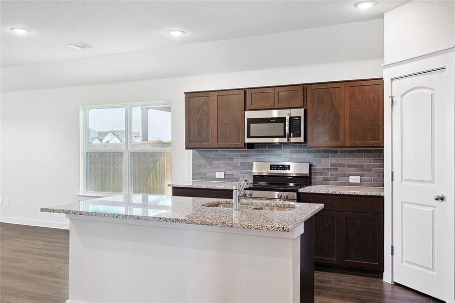 Kitchen featuring dark hardwood / wood-style floors, appliances with stainless steel finishes, an island with sink, sink, and light stone counters