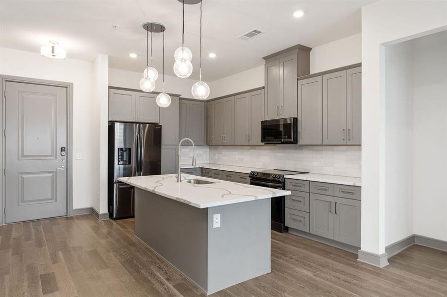 Kitchen featuring stainless steel appliances, wood-type flooring, backsplash, hanging light fixtures, and sink