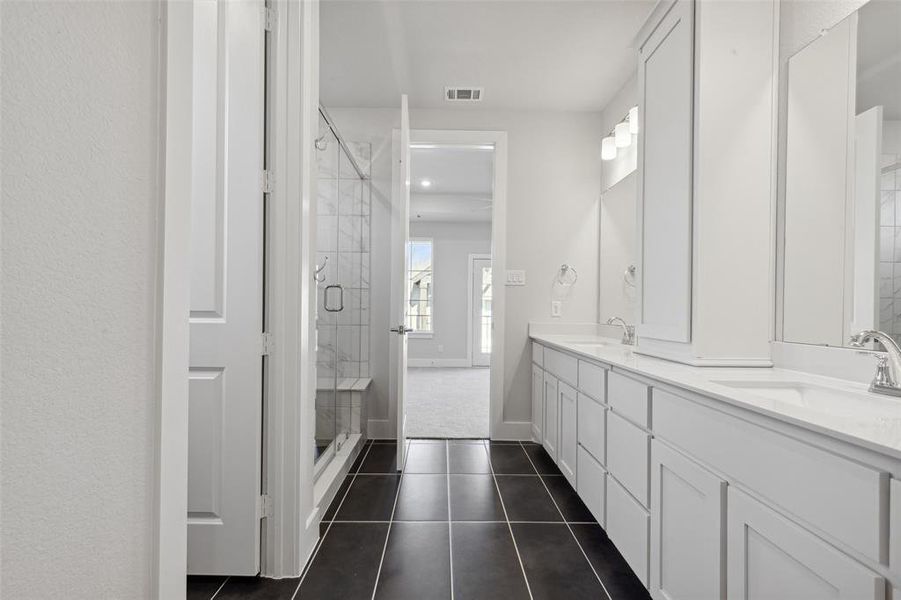 Bathroom featuring dual bowl vanity, tile flooring, and a shower with shower door