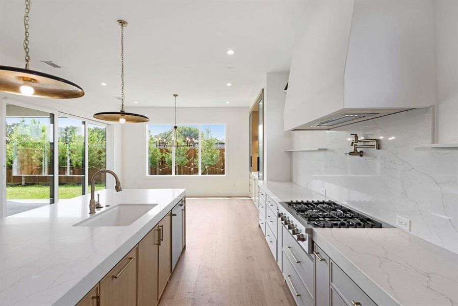 Kitchen with hanging light fixtures, sink, backsplash, light stone countertops, and gas stovetop