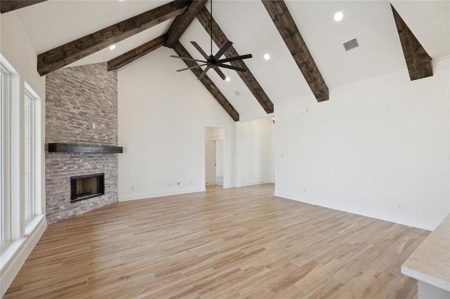 Unfurnished living room with high vaulted ceiling, ceiling fan, light hardwood / wood-style flooring, and a stone fireplace