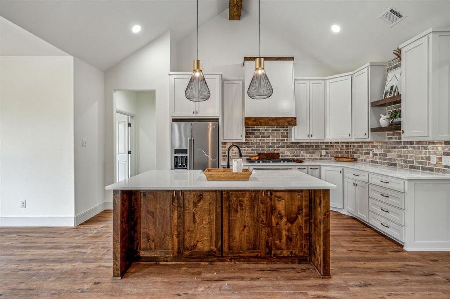 Kitchen featuring high end fridge, wood-type flooring, a kitchen island with sink, and decorative light fixtures