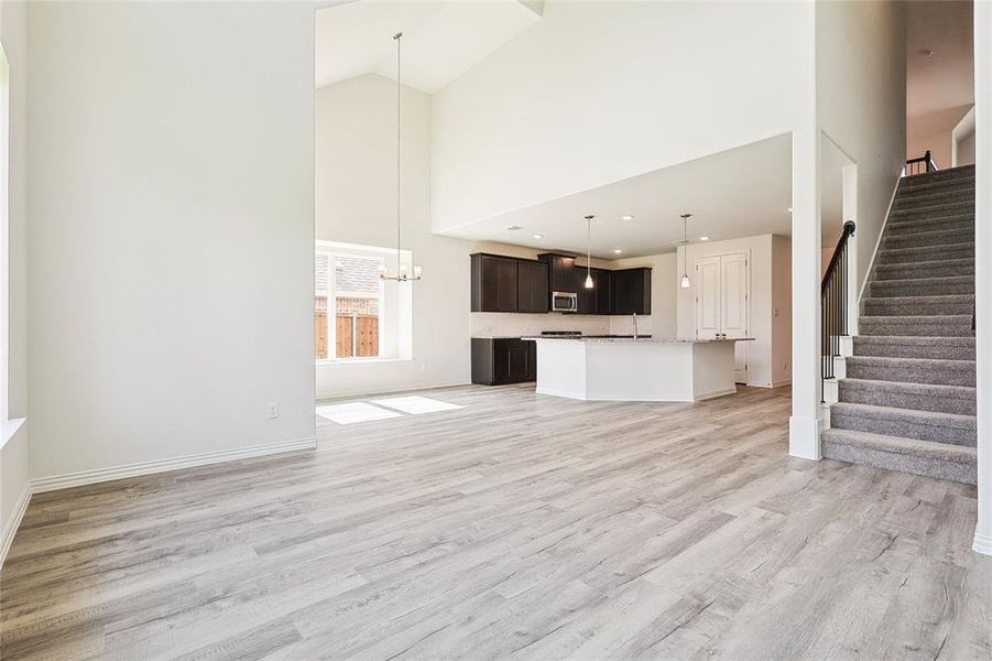 Unfurnished living room featuring light hardwood / wood-style flooring, an inviting chandelier, and high vaulted ceiling