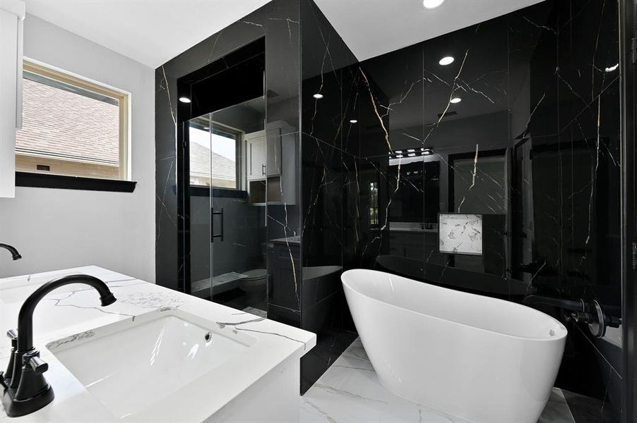 Step into the stunning primary bathroom with modern finishes, where white floor tiles contrast beautifully with luxurious black tiles adorned with gold details on the shower and soaking tub wall from floor to ceiling. Additionally, it includes an inset shower and tub niche for added functionality.