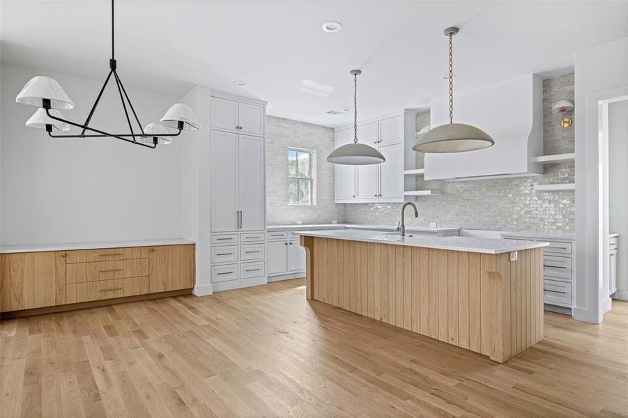 Kitchen featuring backsplash, decorative light fixtures, an island with sink, white cabinets, and light hardwood / wood-style floors