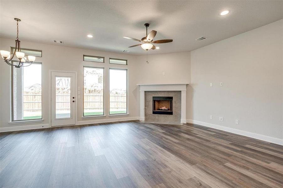 Unfurnished living room featuring ceiling fan with notable chandelier, a fireplace, and dark wood-type flooring