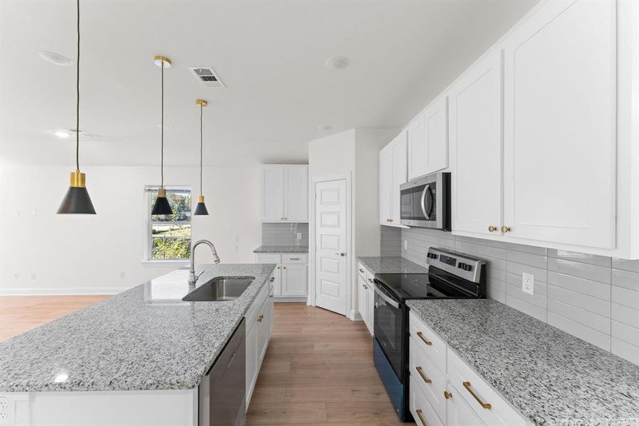 Kitchen featuring an island with sink, white cabinets, pendant lighting, appliances with stainless steel finishes, and light hardwood / wood-style floors