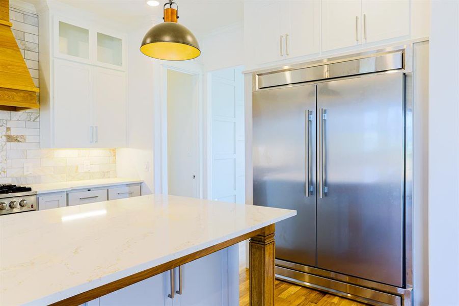 Kitchen featuring tasteful backsplash, built in fridge, hanging light fixtures, light hardwood / wood-style floors, and custom range hood