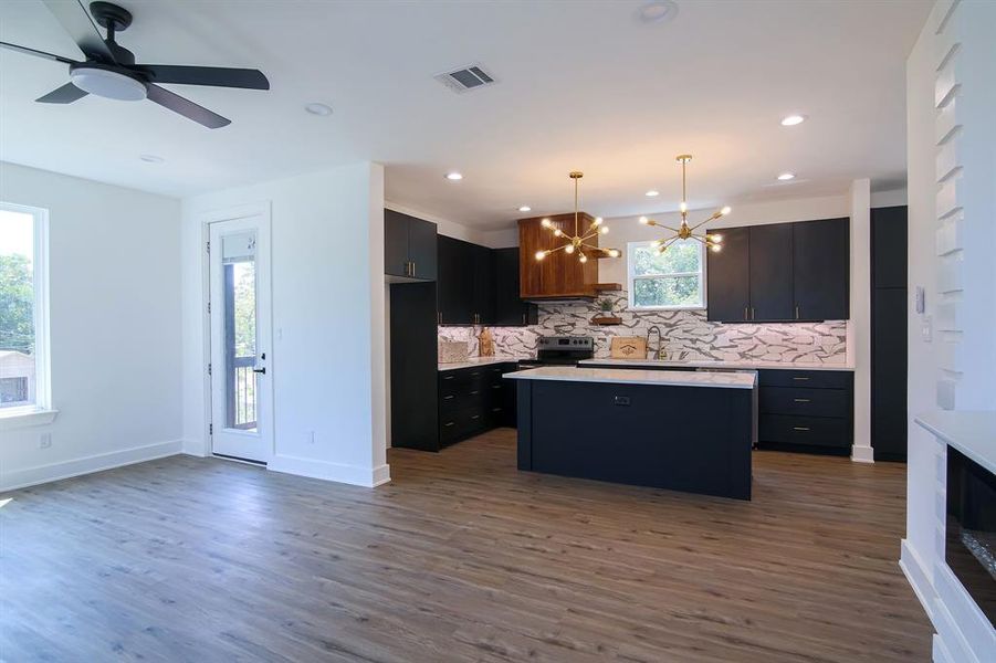 Kitchen with dark wood-type flooring, ceiling fan with notable chandelier, stainless steel range with electric cooktop, a kitchen island, and decorative light fixtures