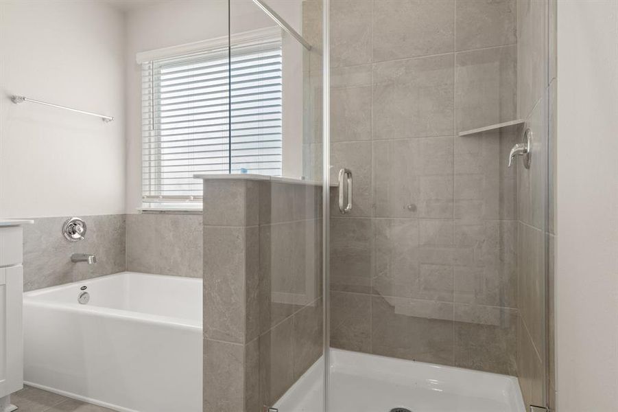 An additional view of the Primary Bath Oasis featuring a glass encased walk-in shower with tile surround, separate soaking tub, water closet for added privacy and oversized window to bring in tons of natural light.