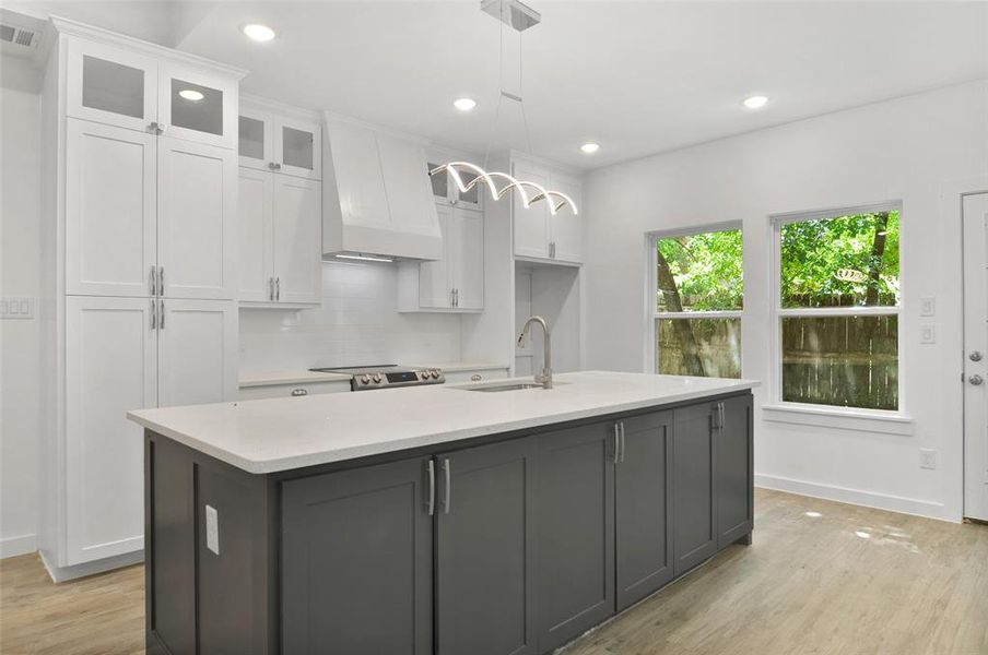 Kitchen with tasteful backsplash, white cabinets, an island with sink, light wood-type flooring, and custom range hood