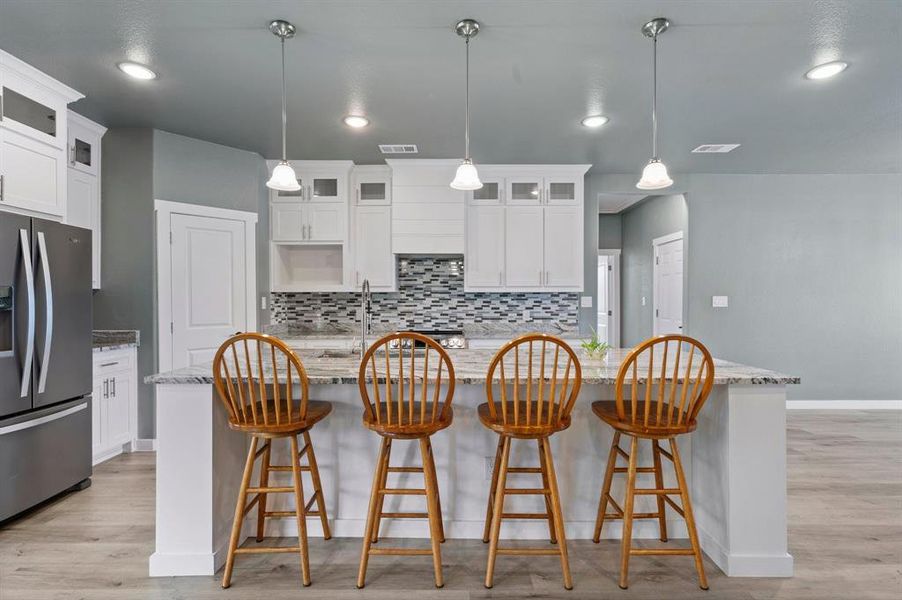 Kitchen with white cabinets, light stone countertops, decorative backsplash, and stainless steel refrigerator with ice dispenser