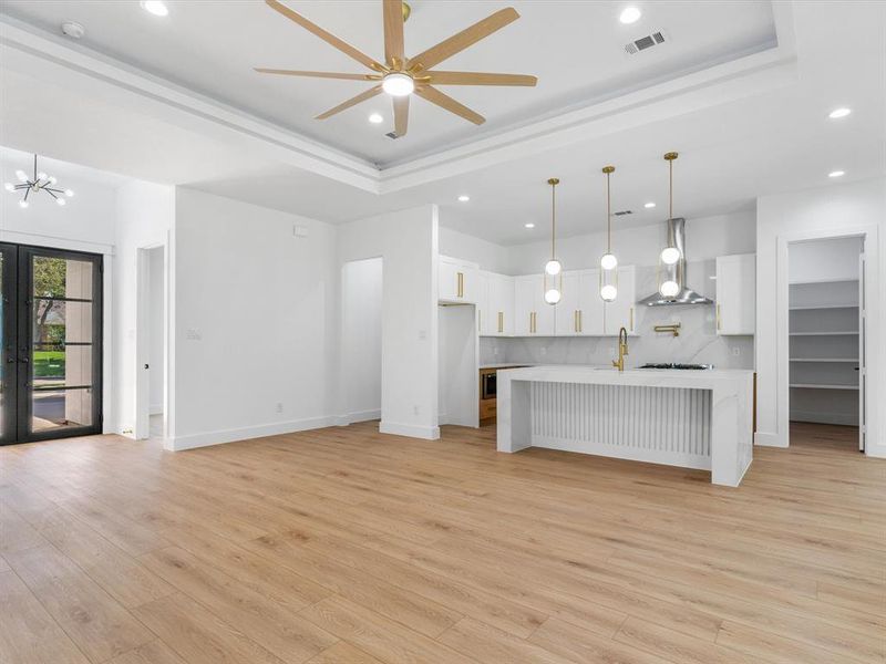 Unfurnished living room with french doors, ceiling fan with notable chandelier, a raised ceiling, and light hardwood / wood-style floors