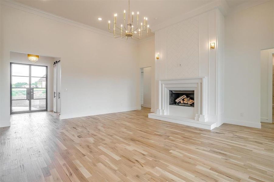 Unfurnished living room with a towering ceiling, light wood-type flooring, and ornamental molding