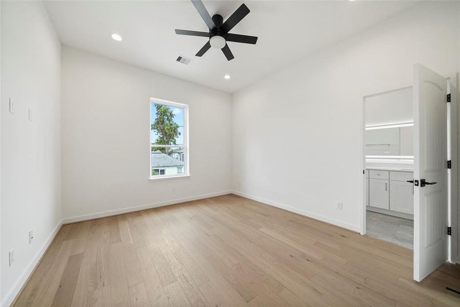 This is a bright, airy room with modern finishes, featuring light hardwood floors, crisp white walls, recessed lighting, a contemporary ceiling fan, and a large window for natural light. There's also a built-in closet or storage area.