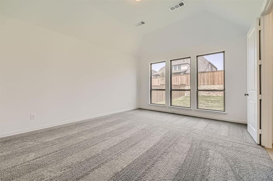 Spare room with a wealth of natural light, vaulted ceiling, and light colored carpet