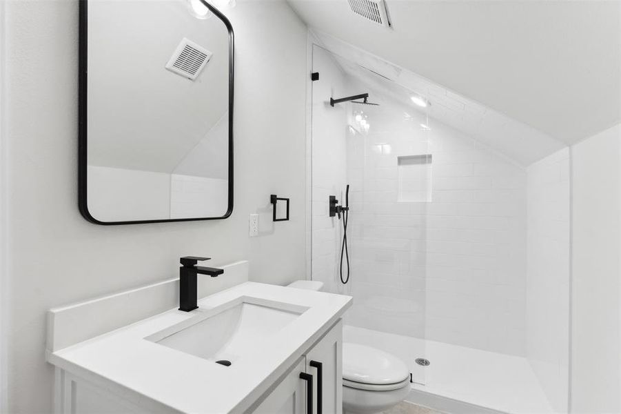 Bathroom featuring a tile shower, vaulted ceiling, vanity, and toilet