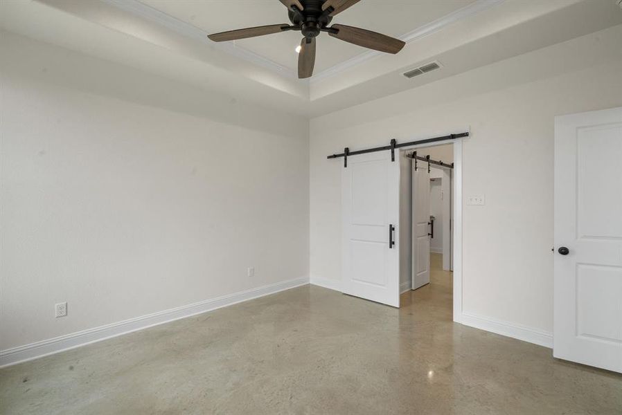 Unfurnished room with ceiling fan, concrete flooring, a raised ceiling, crown molding, and a barn door