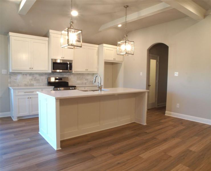 Kitchen featuring decorative light fixtures, an island with sink, stainless steel appliances, sink, and white cabinets