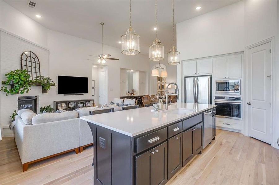 Kitchen with high vaulted ceiling, white cabinetry, a kitchen island with sink, and appliances with stainless steel finishes