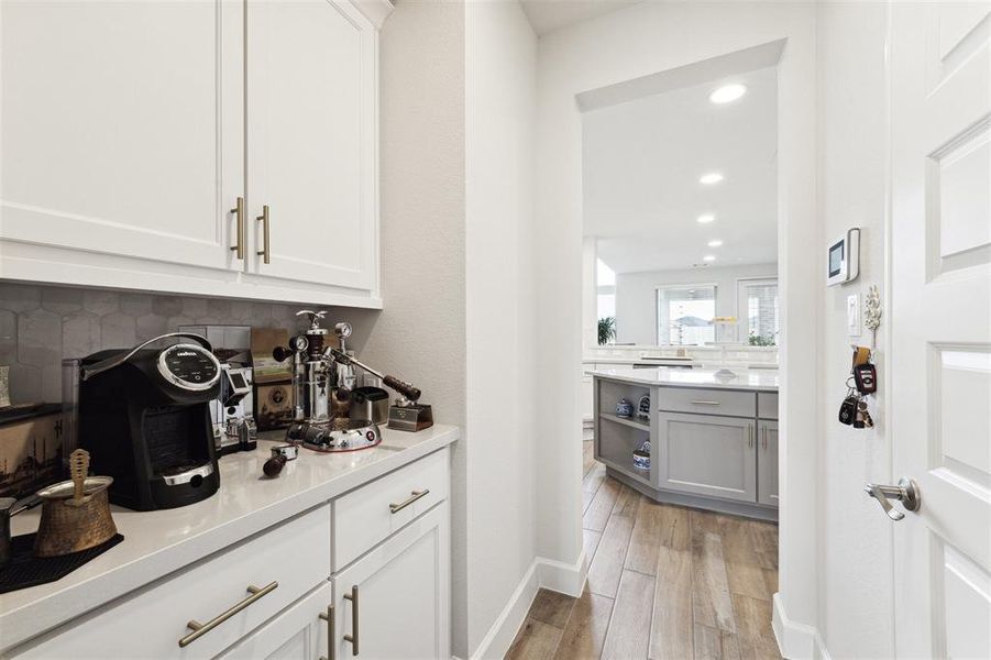 The butler pantry features a custom tile backsplash, quartz counter top and upper and lower level cabinet storage.