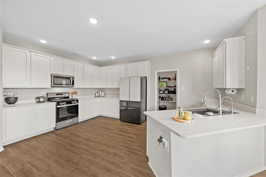 Kitchen with hardwood / wood-style flooring, stainless steel appliances, white cabinets, sink, and kitchen peninsula