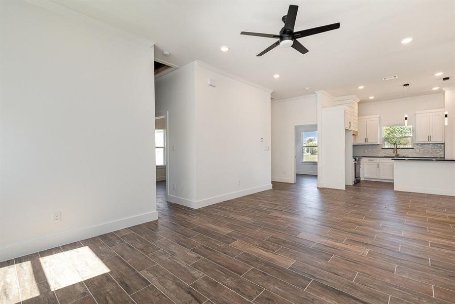 Unfurnished living room with ornamental molding, ceiling fan, and dark hardwood / wood-style flooring