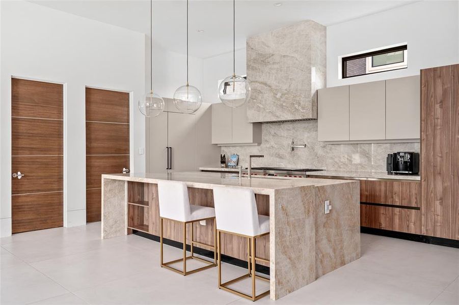 This modern kitchen showcases an expansive waterfall island with sleek Taj Mahal quartzite countertops that extend gracefully down the sides, providing both a functional workspace and a bold design statement.