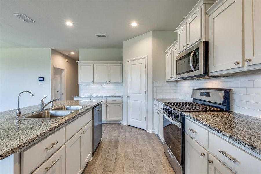 Kitchen featuring light wood-type flooring, sink, white cabinetry, decorative backsplash, and stainless steel appliances