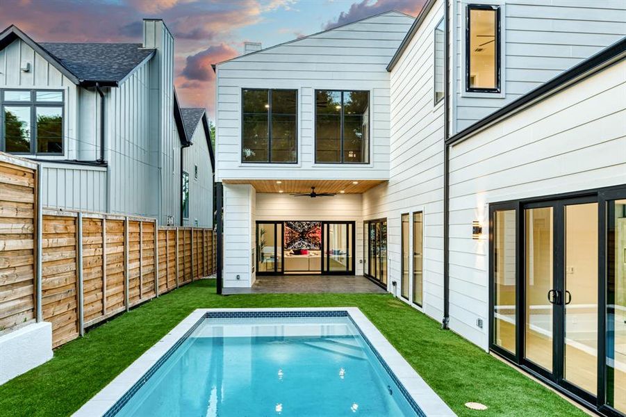 Back house at dusk featuring ceiling fan and a fenced in pool