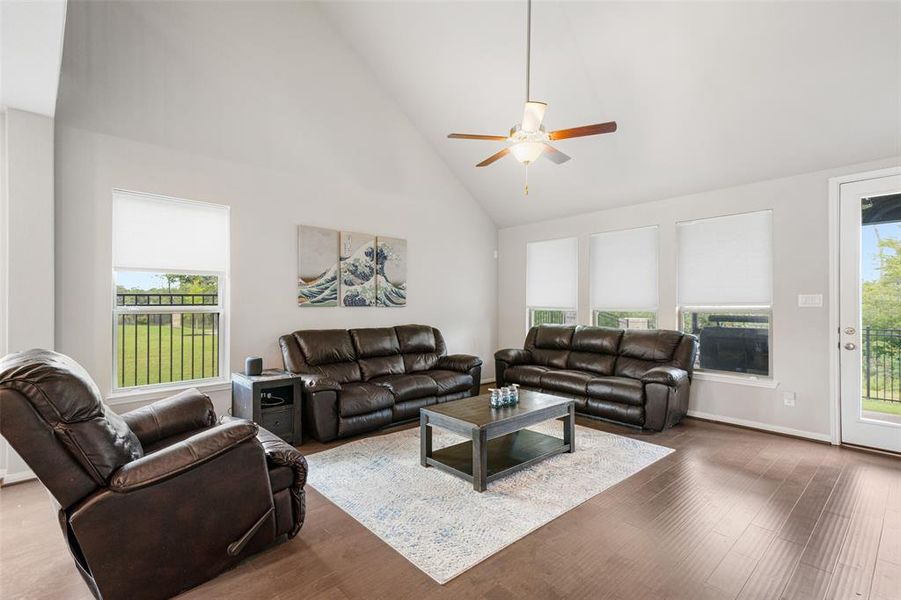 What a spacious living room with high vaulted ceilings, large windows allowing for plenty of natural light, and a glass paned door leading to the covered back patio & backyard space. The hardwood flooring adds warmth to the space!