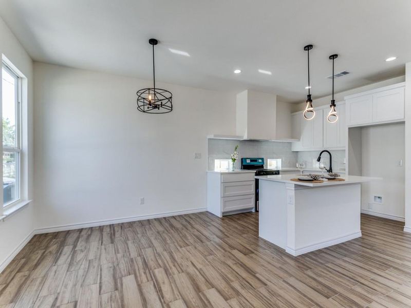 Kitchen featuring hanging light fixtures, light wood-type flooring, a center island with sink, and white cabinets