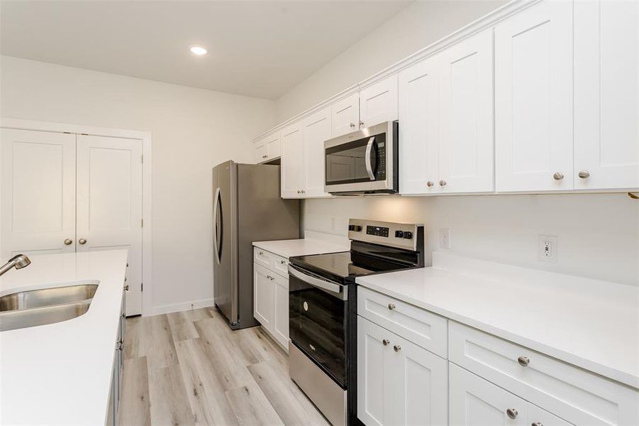 Kitchen with appliances with stainless steel finishes, white cabinetry, sink, and light wood-type flooring