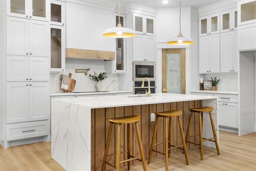 Kitchen with white cabinets, decorative light fixtures, a center island with sink, and light wood-type flooring