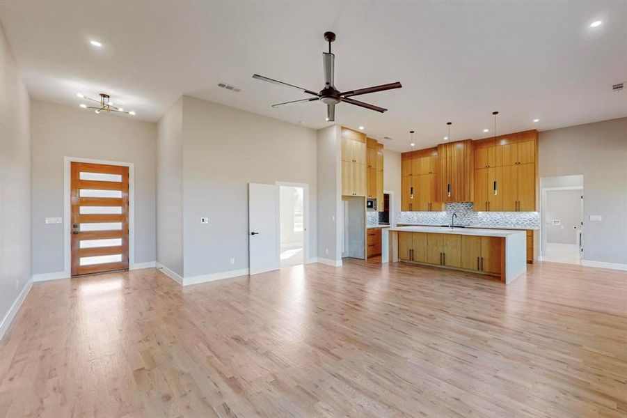 Kitchen with a center island with sink, backsplash, light wood-type flooring, ceiling fan with notable chandelier, and decorative light fixtures