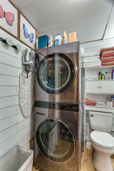 Clothes washing area featuring light hardwood / wood-style floors, stacked washer / dryer, and wood walls