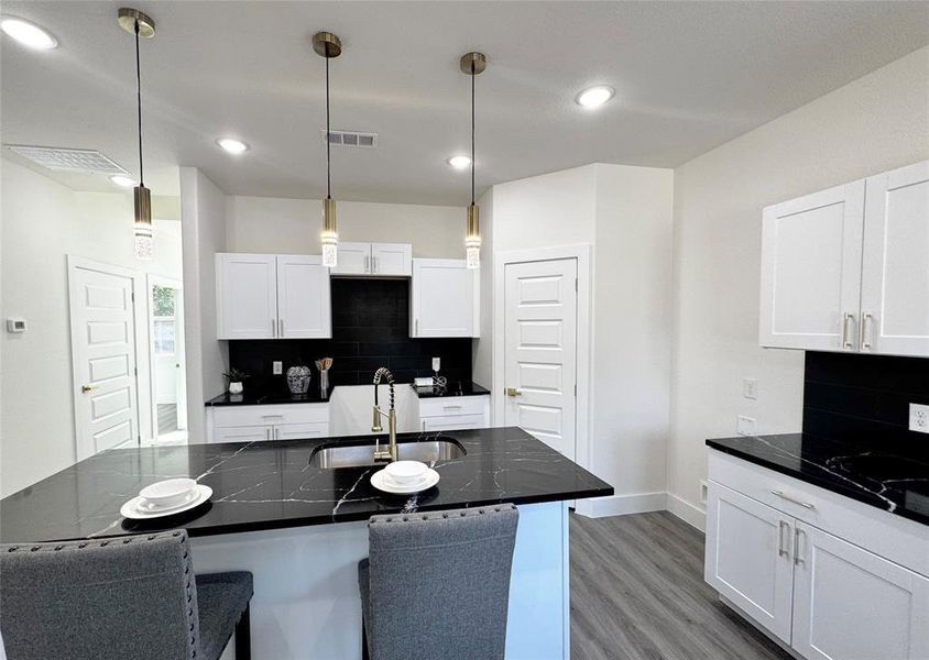 Kitchen featuring dark stone counters, decorative light fixtures, sink, and white cabinets