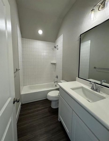 Full bathroom with vaulted ceiling, vanity, hardwood / wood-style flooring, toilet, and tiled shower / bath