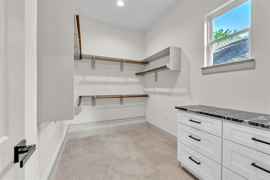 Large walk-in-closet with a built-in-shelves, hanging rods, a widow, and a set of drawers with a granite countertop