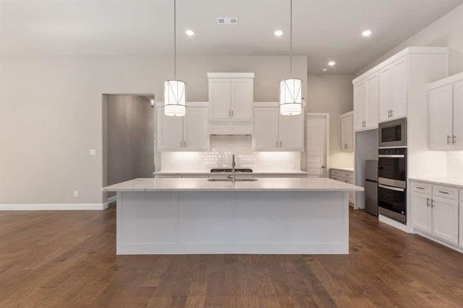 Kitchen featuring pendant lighting, an island with sink, and dark wood-type flooring