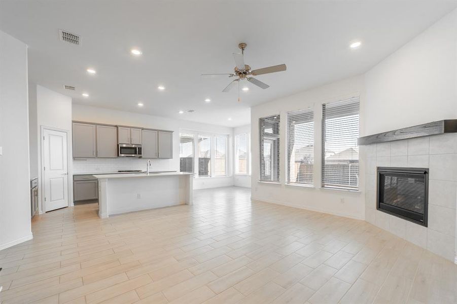 Unfurnished living room featuring sink, light wood-type flooring, a fireplace, and ceiling fan