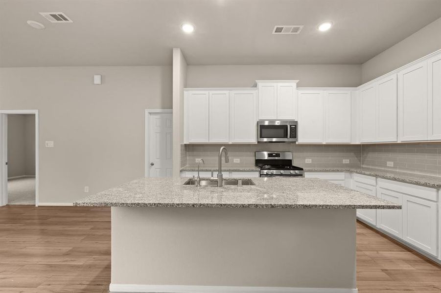 This light and bright kitchen features a large quartz island, white cabinets, a large sink overlooking your family room, recessed lighting, and beautiful backsplash.