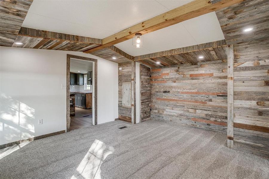 Carpeted empty room with wood walls and vaulted ceiling with beams