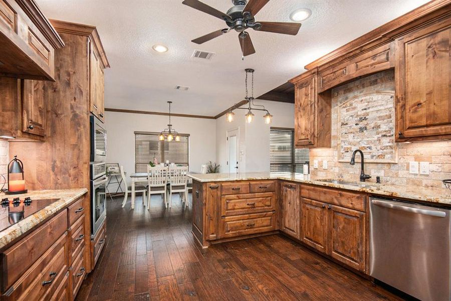 Kitchen featuring dark wood-type flooring, kitchen peninsula, stainless steel appliances, sink, and pendant lighting