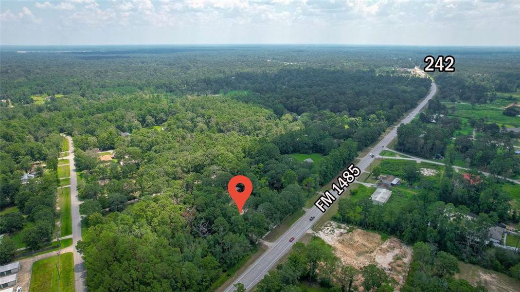 This aerial image showcases a property marked by a red location pin, situated near the intersection of FM 1485 and Highway 242, with easy access to main roads.