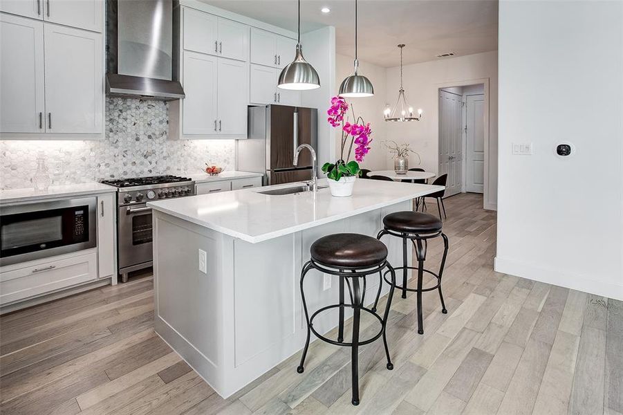 Kitchen featuring light hardwood / wood-style floors, a center island with sink, white cabinetry, wall chimney exhaust hood, and appliances with stainless steel finishes